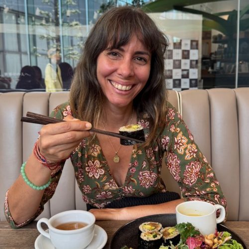 Diana Chiu Baptista, fundadora da Macro Viagens. sorri para a fotografia, com uns pauzinhos e sushi vegetariano