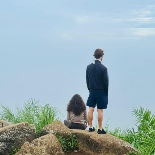 Casal de costas numa montanha, observa paisagem ao nascer do dia