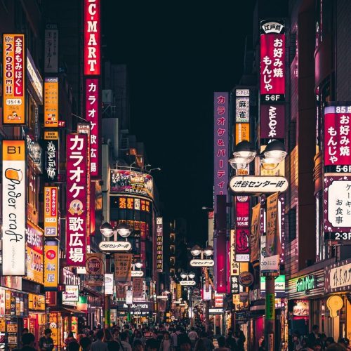 Vista para uma metropole japonesa à noite com prédios, luzes, outdoors electronicos