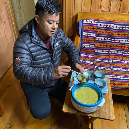 Homem butanês vestido de forma informal serve dhal para taças em casa de uma família