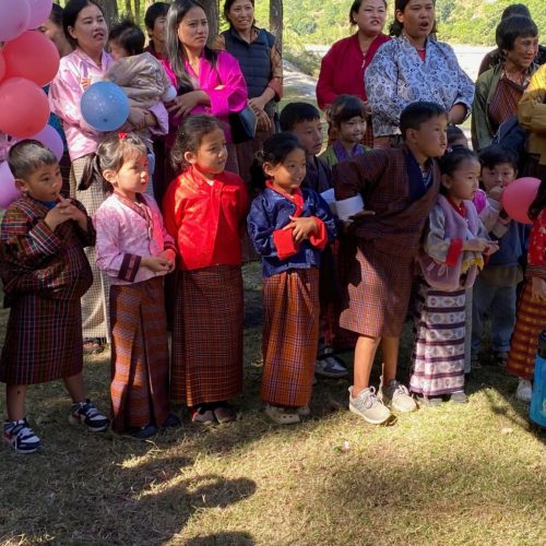 Muitas crianças butanesas juntas, com as suas mães por trás, numa festa de aniversário de uma delas