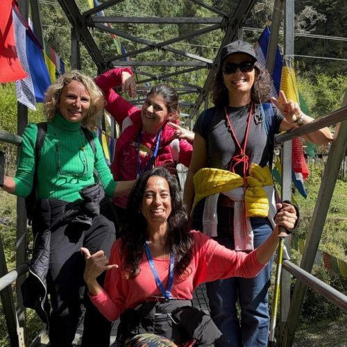 Grupo de 4 mulheres divertidas junto à entrada de uma ponte pedonal suspensa do butão
