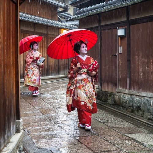 Duas geishas nas ruas de Kyoto com sombrinhas vermelhas e trajes tradicionais