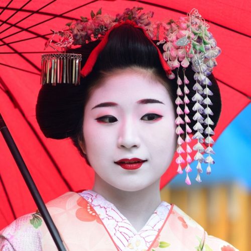 Rosto de uma geisha com maquilhagem branca e uma sombrinha vermelha