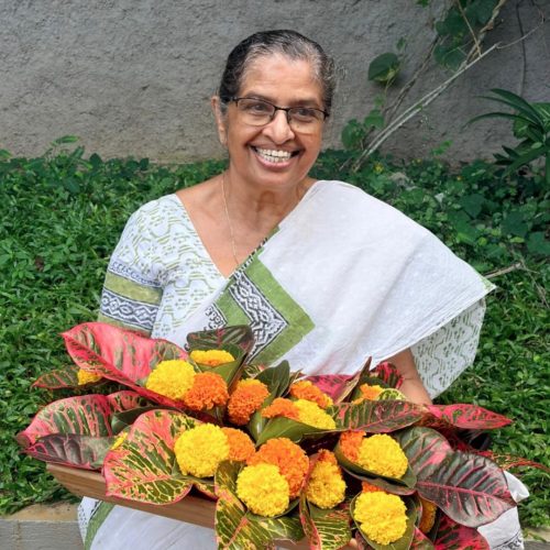 Molly Joy, matriarca da família Madukkakuzhy sorridente com flores para receber os hóspedes