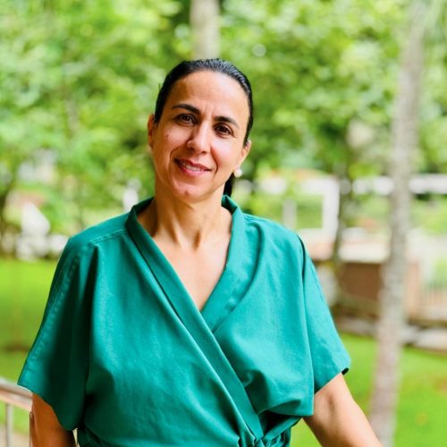Senhora ocidental sorri para fotografia, vestida com robe para tratamentos ayurveda