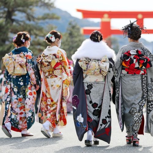Quatro mulheres japonesas vestidas de Komonos, passeiam com um tori vermelho ao fundo