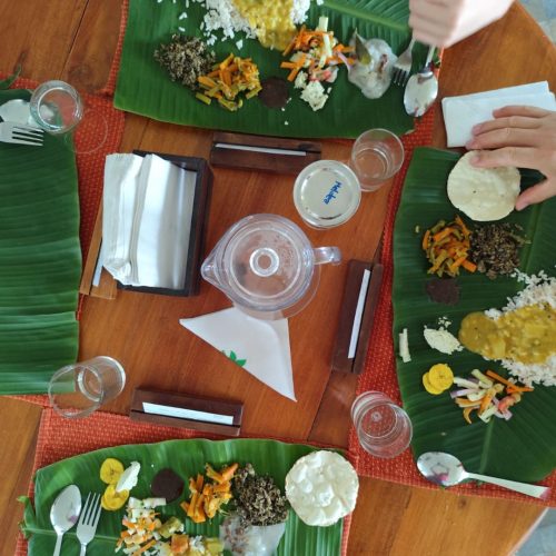 Vista de cima para mesa de refeições onde estão 4 folhas de palmeira com comida do sul da Índia (Sadhya)