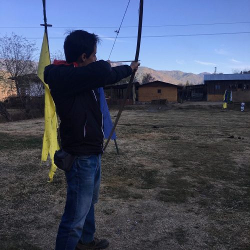 Homem experimenta o tiro ao arco, o desporto tradicional Butanês, num campo ao final do dia