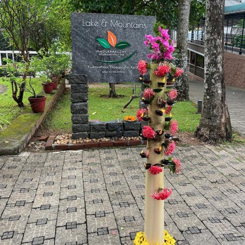 Vista para a entrada no Lake & Mountains onde aparece placa com o nome e um castiçal grande típico de kerala com velas para receber novos hóspedes